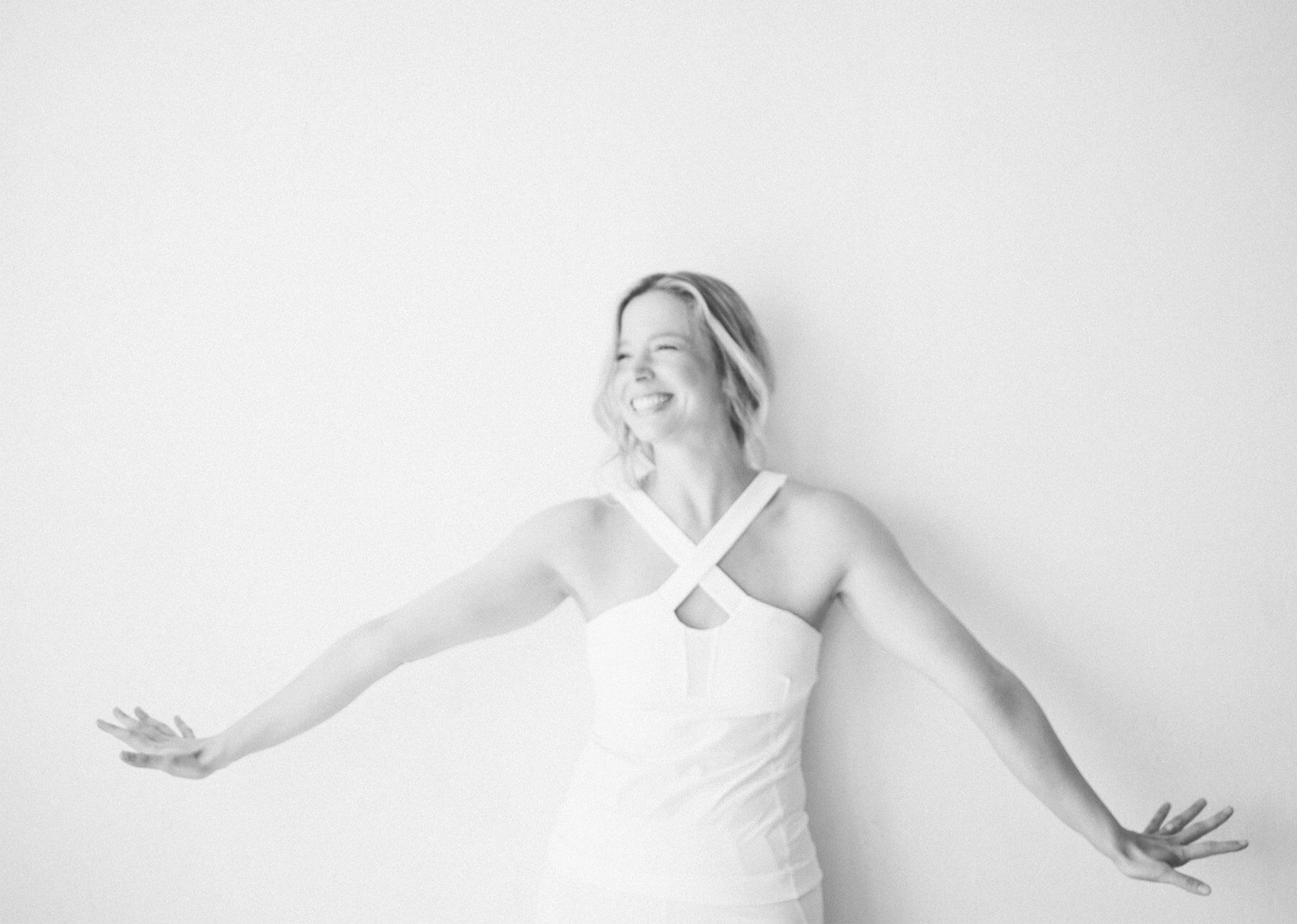 black and white photo of woman with arms stretched out smiling, wearing white top