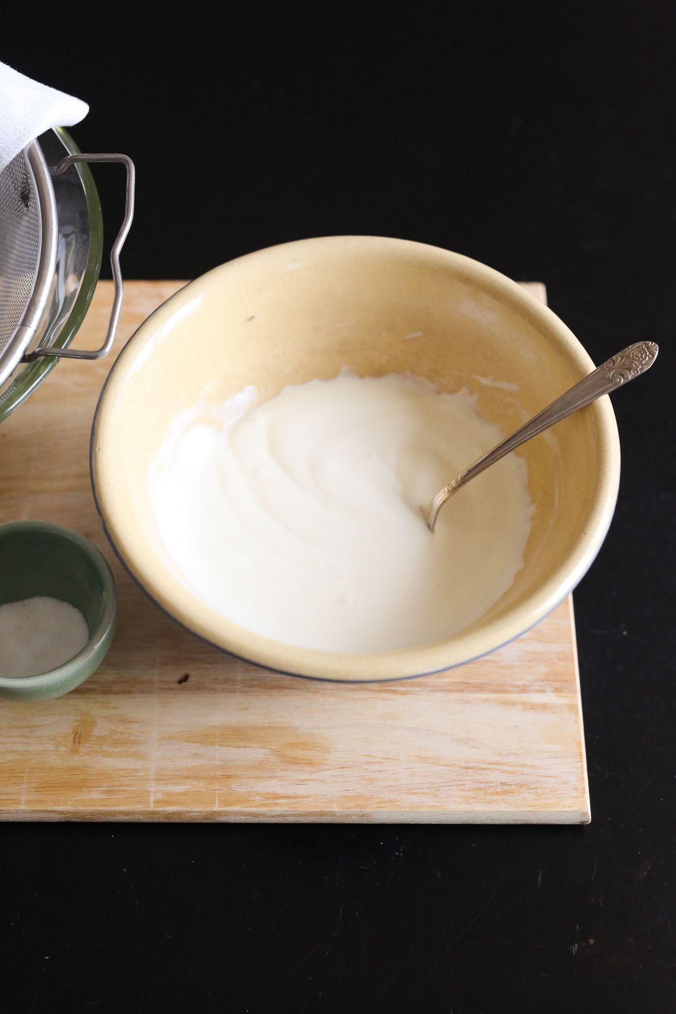 bowl of yogurt with silver spoon on cutting board sitting on black table