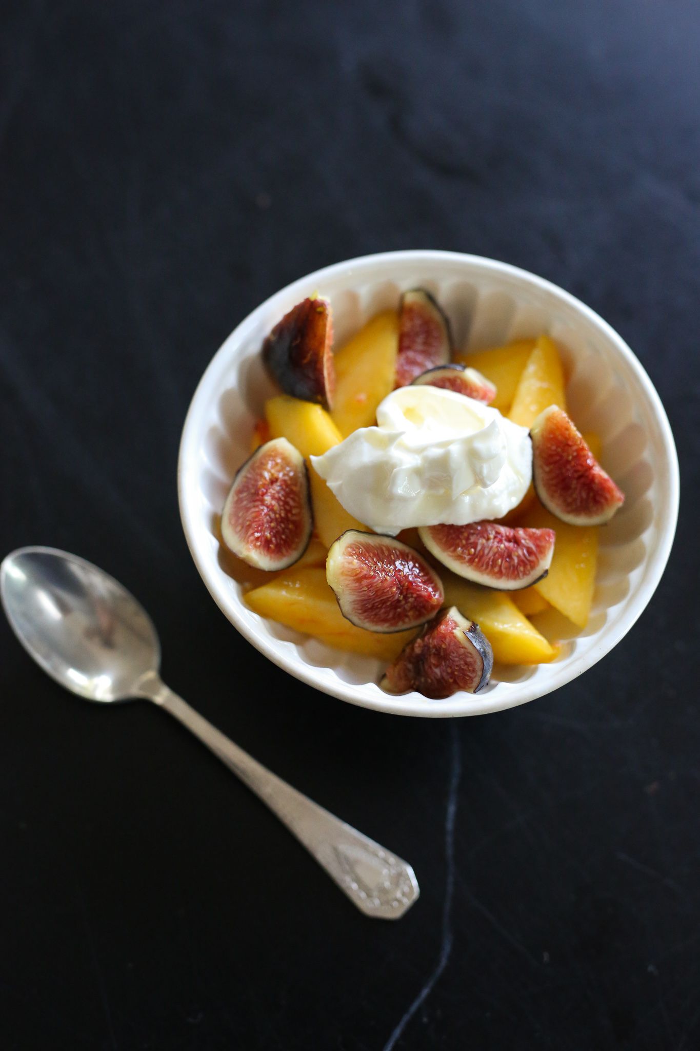 white bowl with silver spoon with peaches and figs and honey on black table