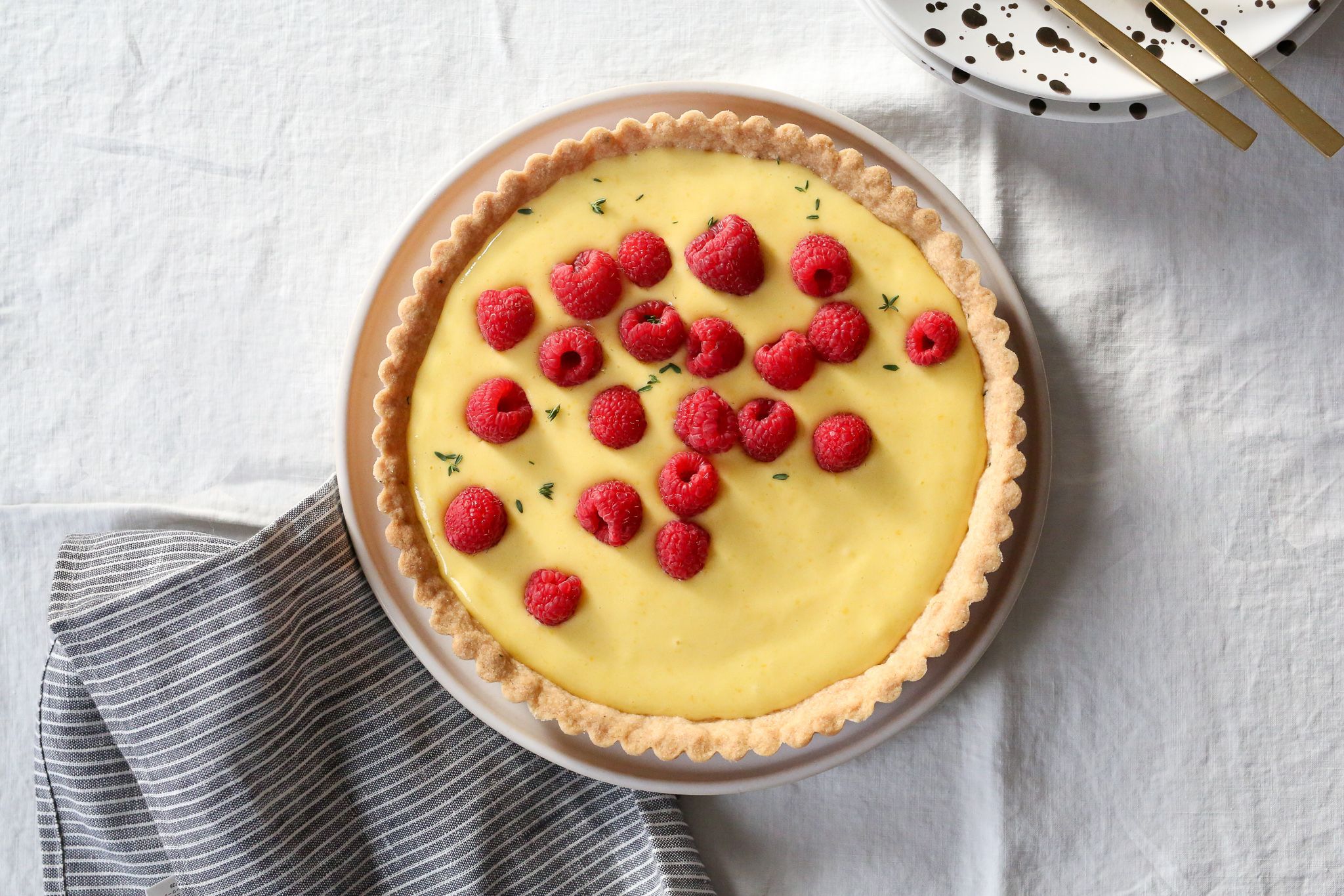 lemon and raspberry tart with grey napkin and brown speckled plate