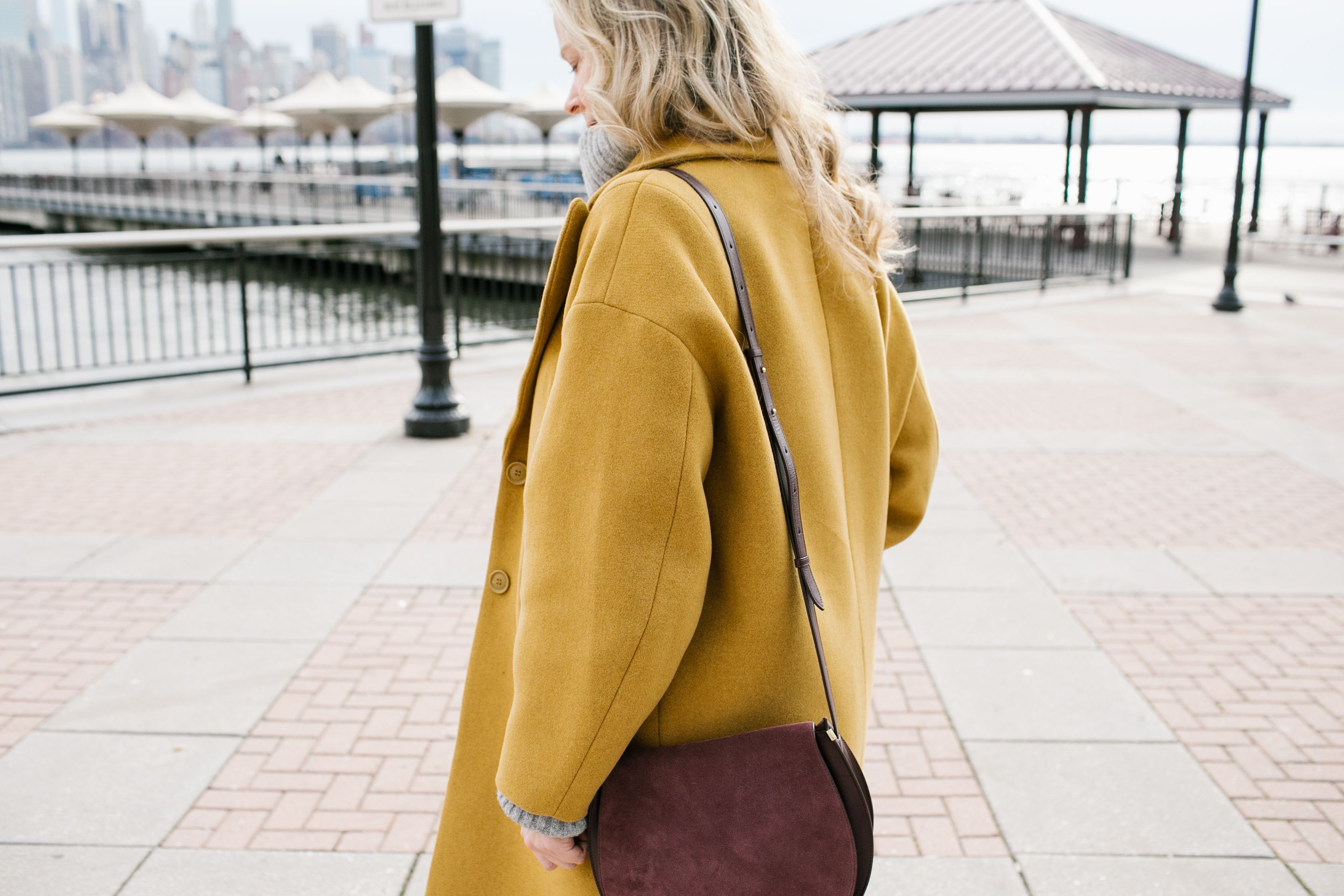 woman in yellow coat with purple bag standing on pier