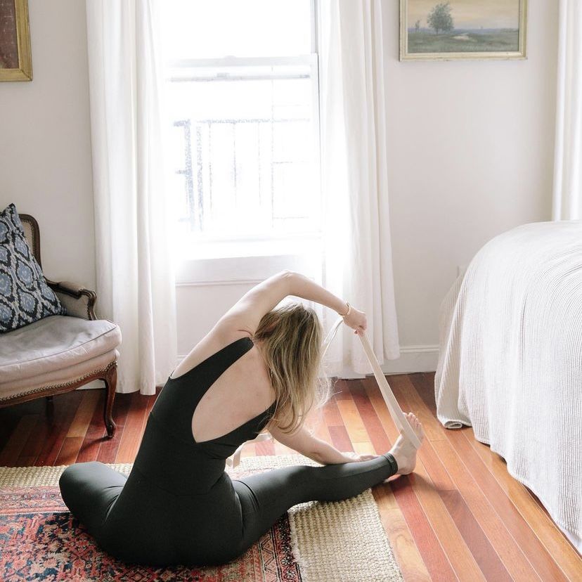woman doing yoga pose in grey unitard in a bedroom