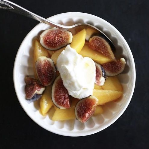 white of bowl of peaches and figs with dollop of labne on a black table with a silver spoon