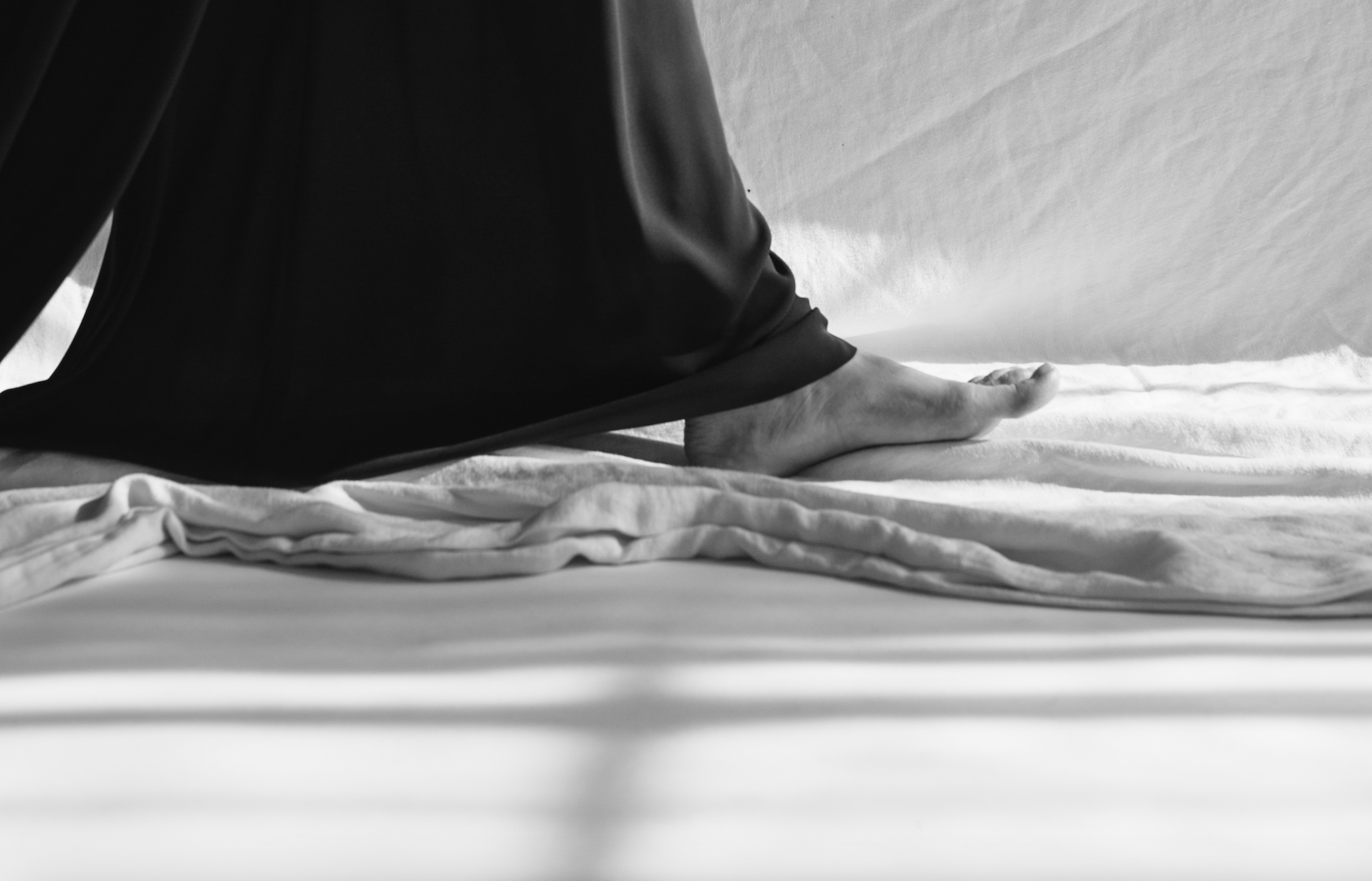black and white image of feet walking on cloth draped on floor, woman is wearing wide-legged flowing pants