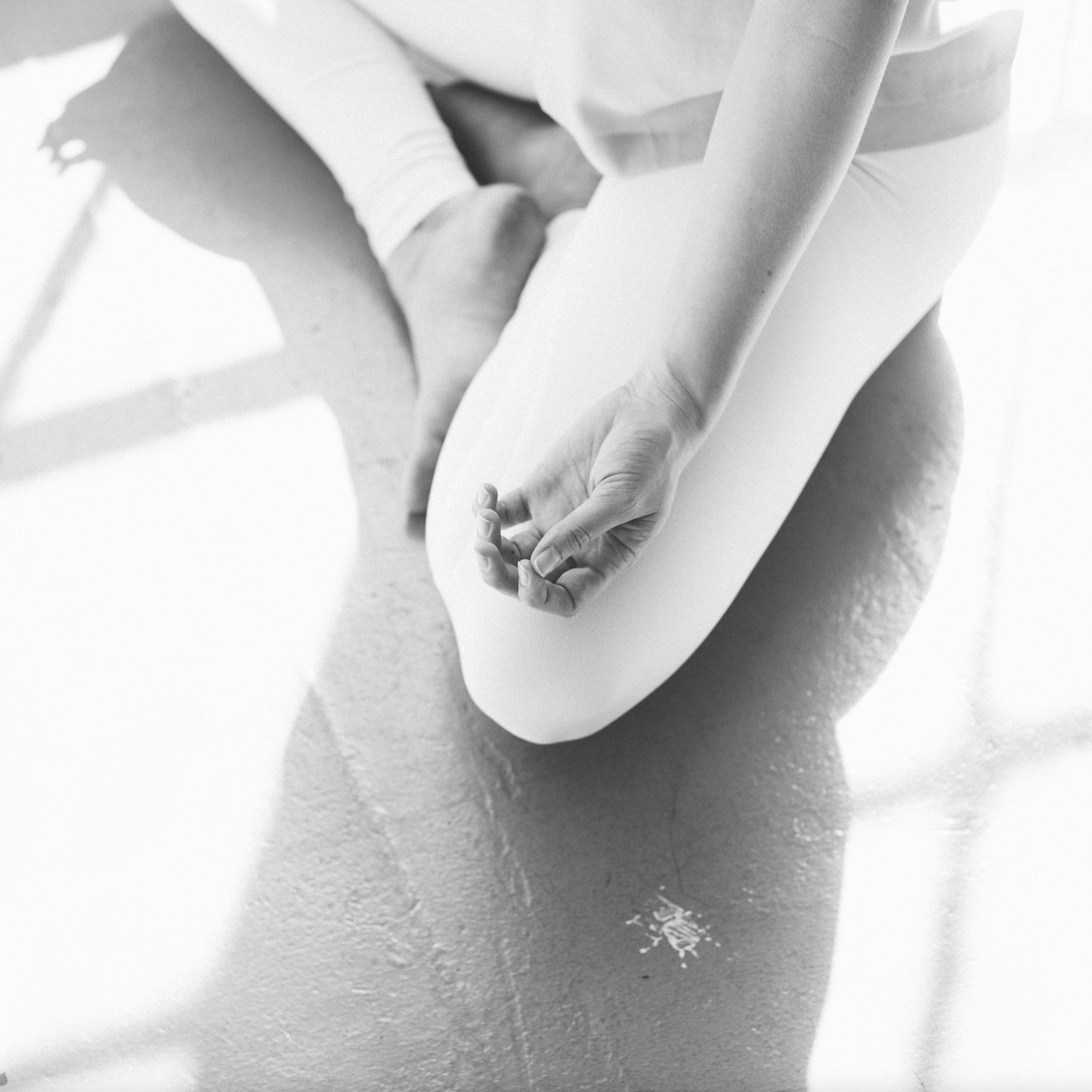 black and white image of cross-legged seat with woman's hand in yoga mudra, shadows of window panes reflected on floor