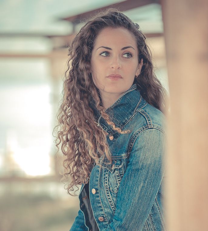 portrait of woman wearing jean jacket with brown curly hair looking off into the distance