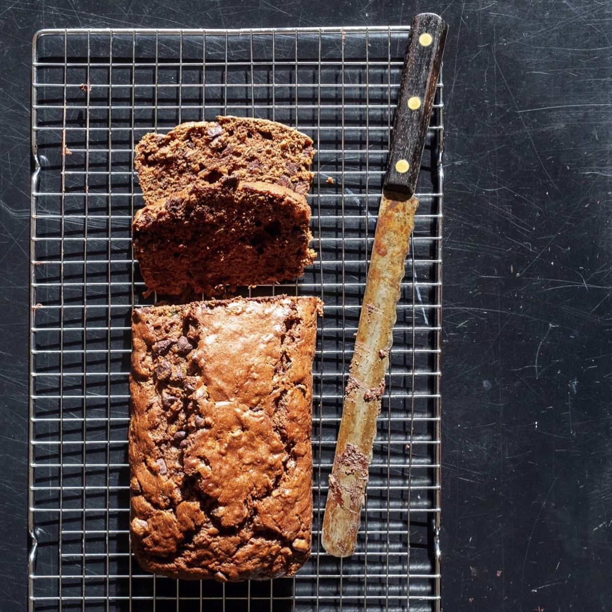 chocolate zucchini bread on cooling rack with old bread knife on top of black table