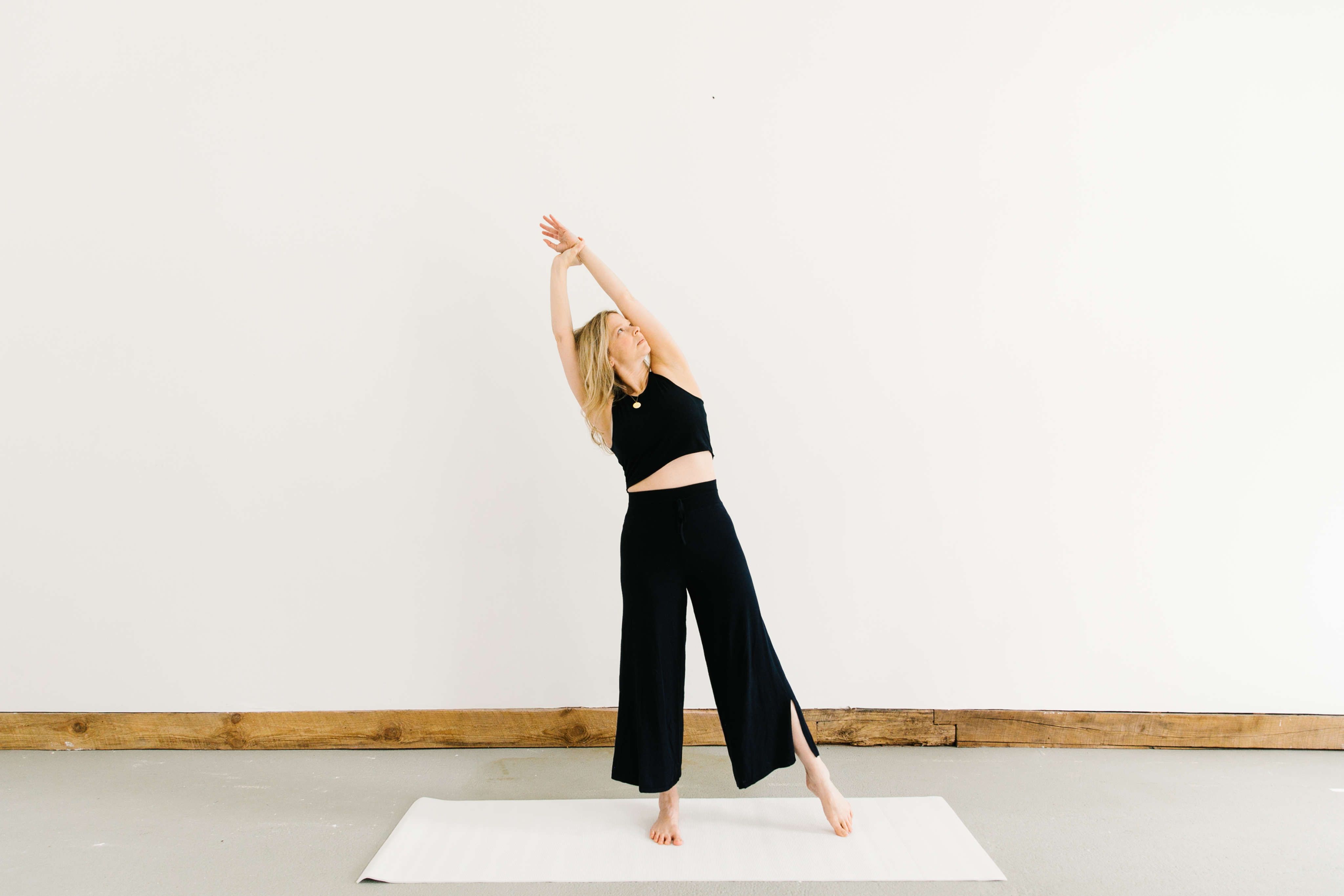 woman practicing stretch wearing blue on white mat against white wall