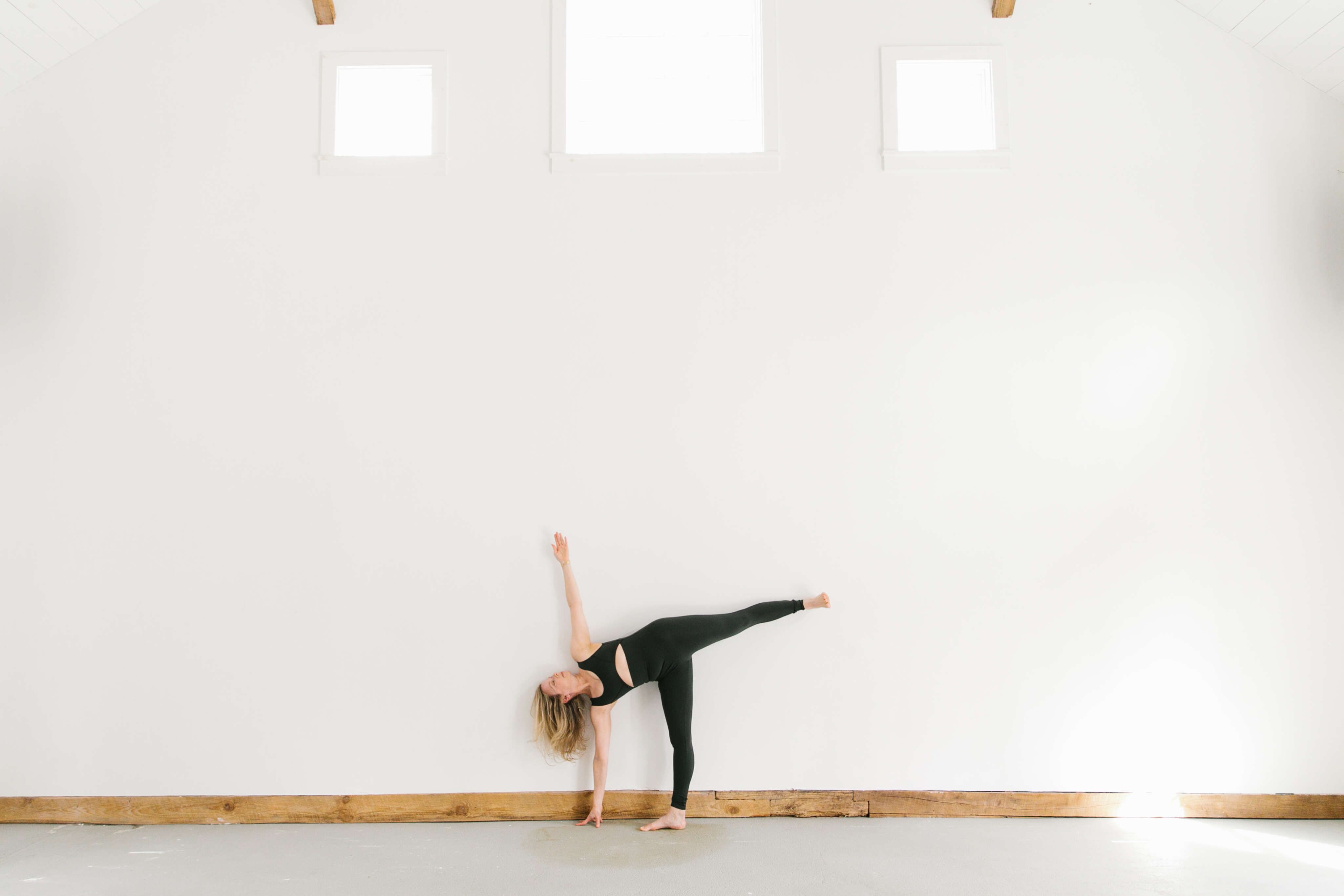 woman doing Half Moon yoga pose in big white space with three windows at top
