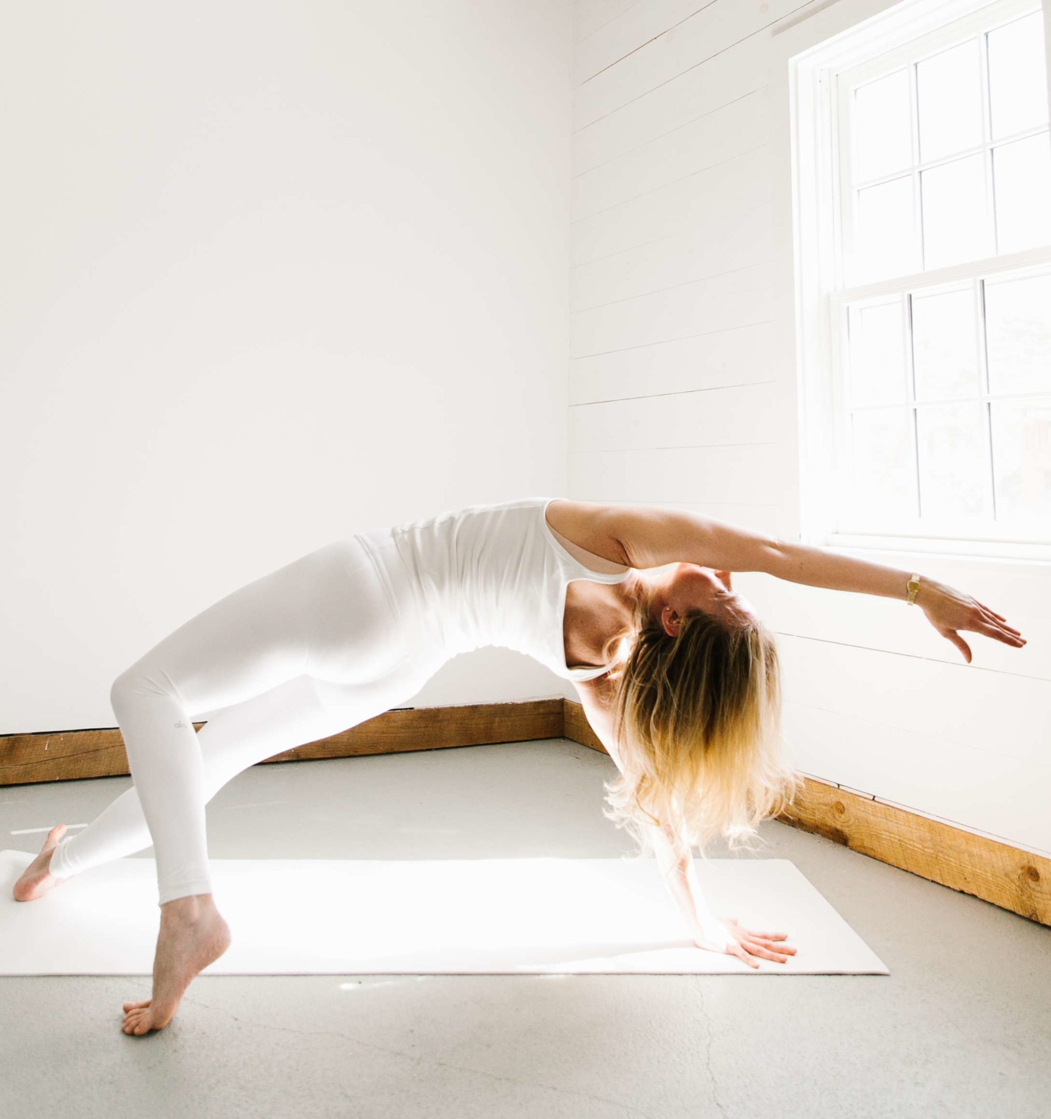 woman practicing a yoga pose called Wild Thing wearing white in a white space