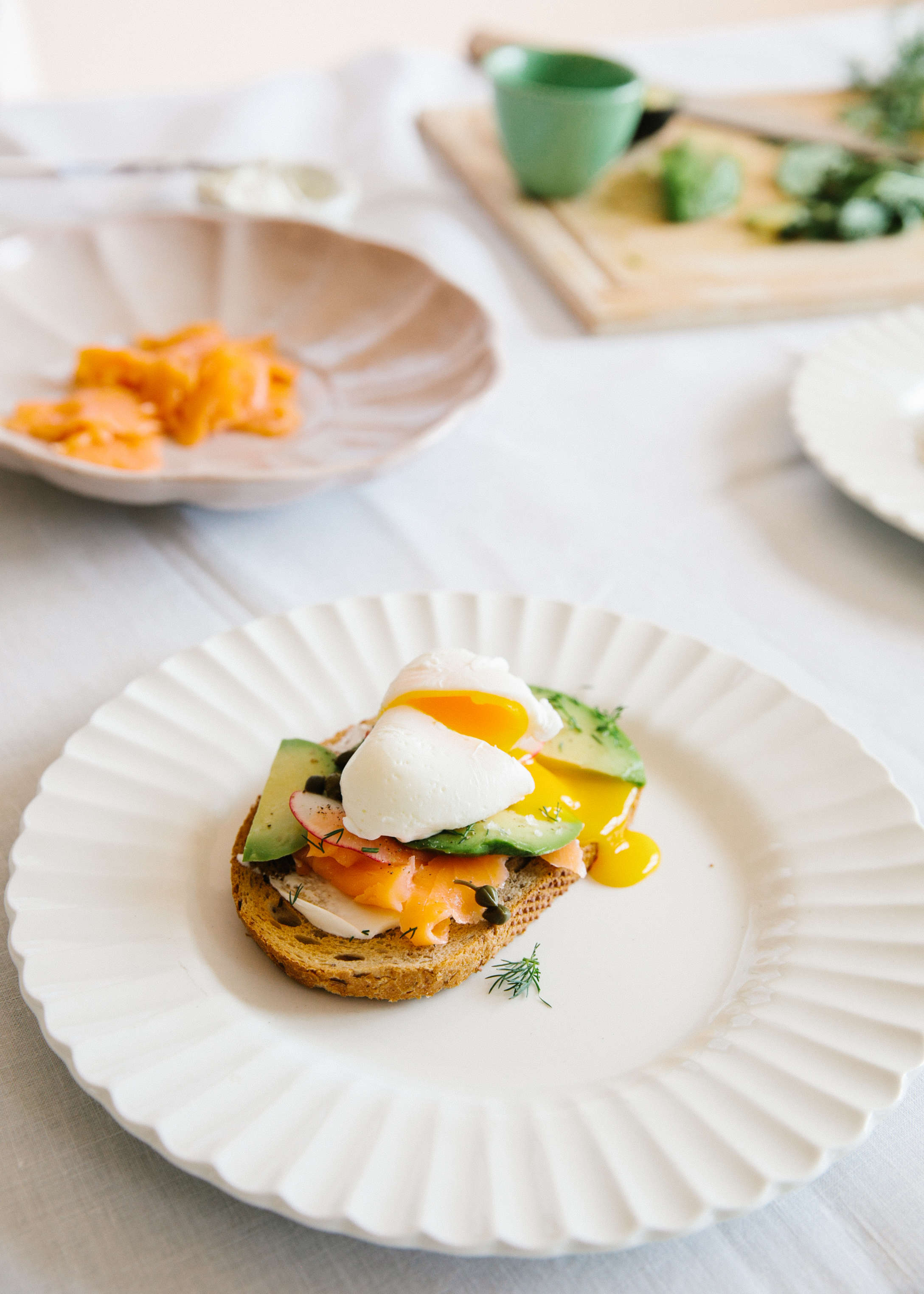 white plate with tartine of salmon, avocado, and radishes topped with poached egg