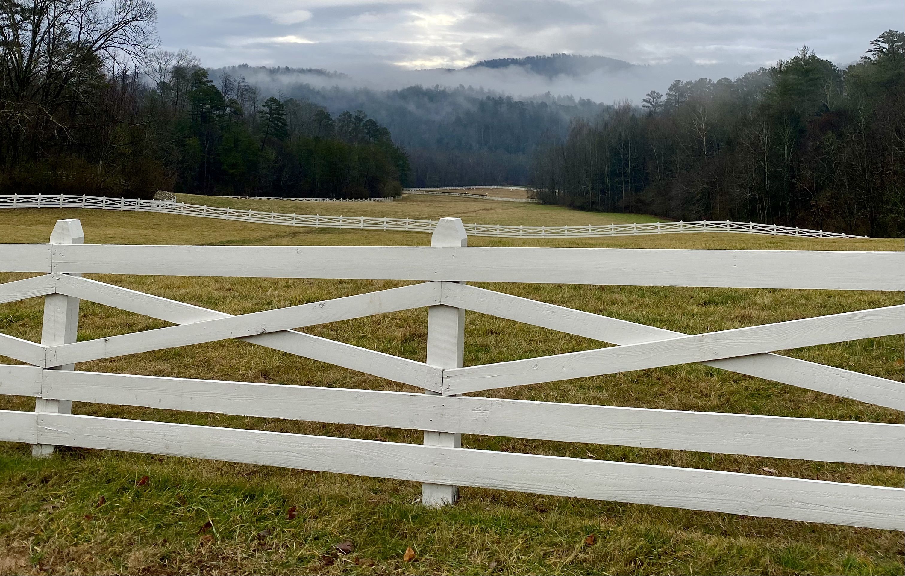 white wooden fence with rolling hills, mountains, and foggy skies