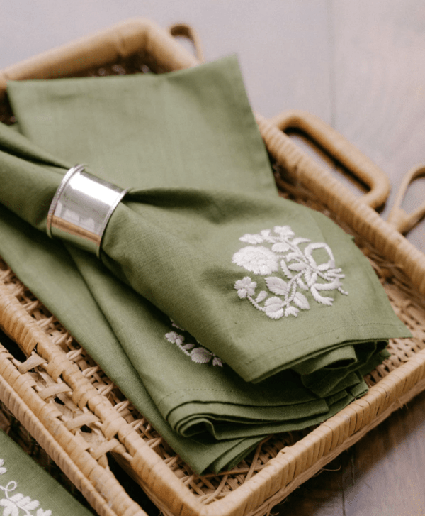 green napkin with white embroidery in silver napkin ring sitting in a wicker basket