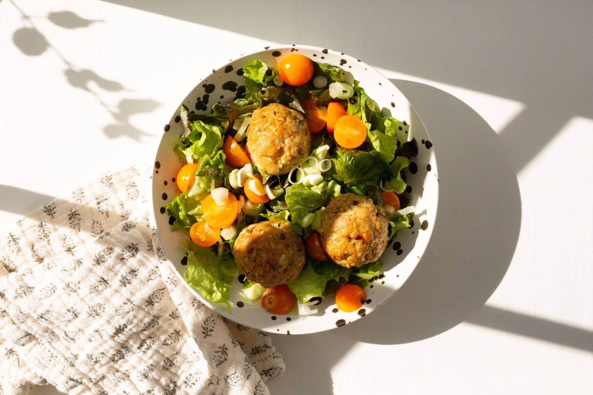 bowl of salad with turkey meatballs on white table with white printed napkin