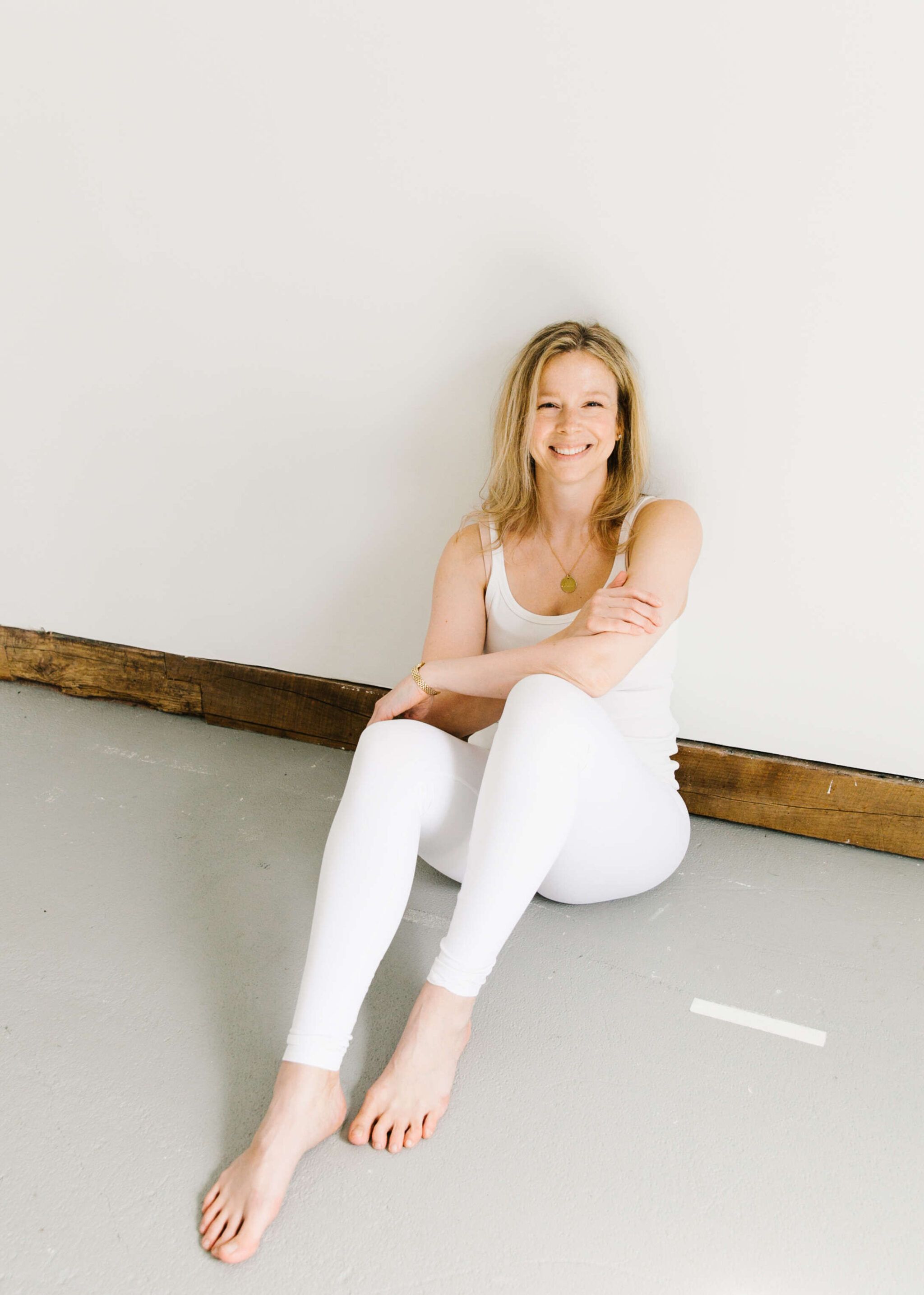 woman wearing white sitting on grey concrete floor smiling